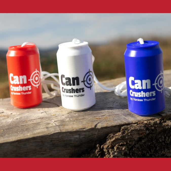 Three small toy objects shaped like soda cans stand on a wooden surface. The cans are red, white, and blue, each labeled 