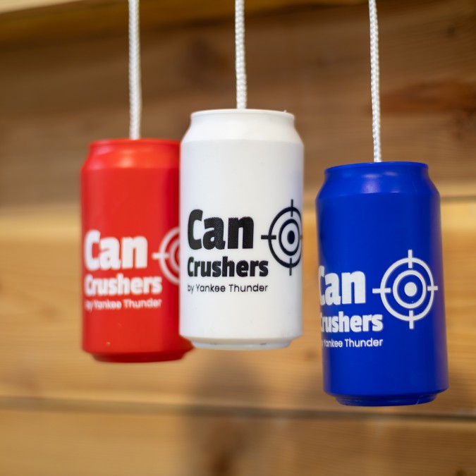 Three hanging can crushers in red, white, and blue colors are displayed against a wooden background. Each durable and reusable crusher has 