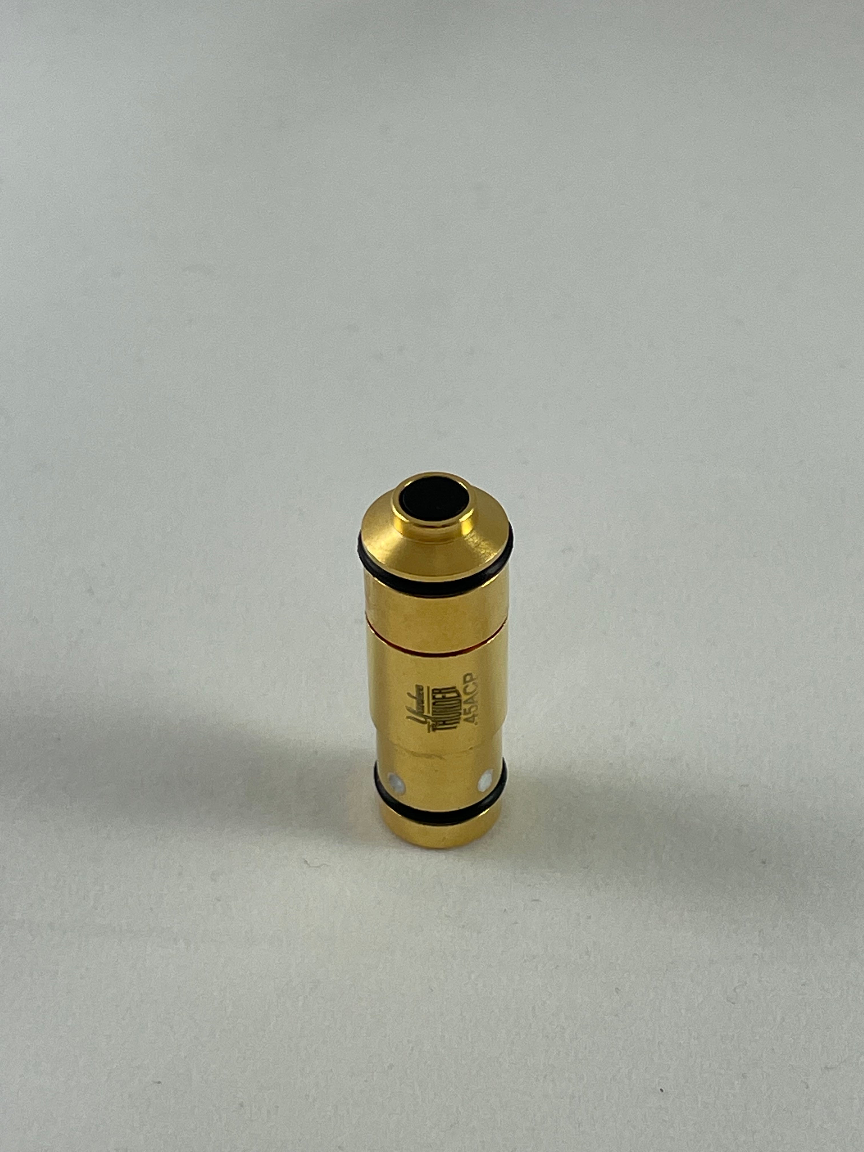 A small .380 Laser Cartridge by Yankee Thunder, gold-colored and cylindrical with black rings on both ends and text and markings on its surface, stands upright on a white background, resembling a laser cartridge used for dry-fire practice.
