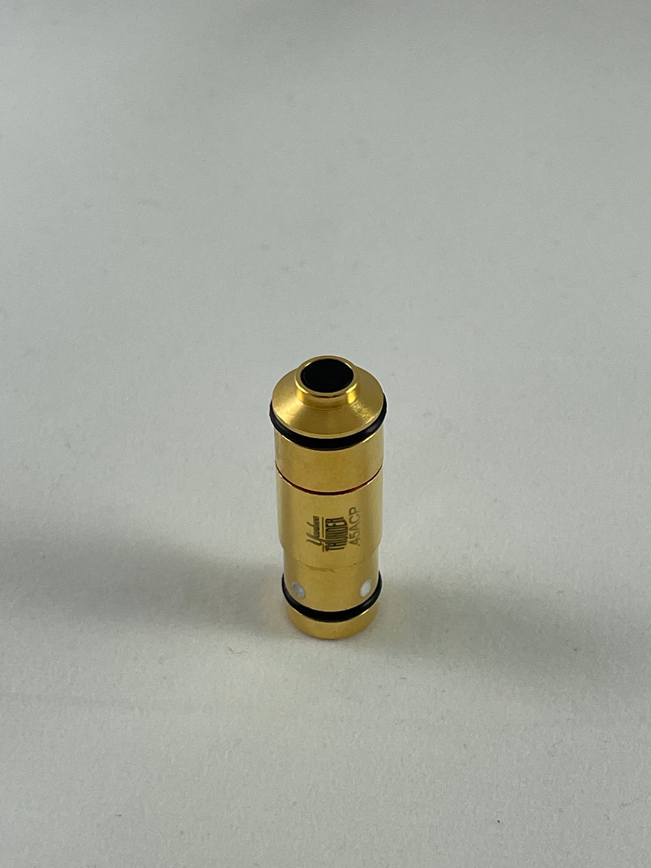 A cylindrical .45 Laser Cartridge from Yankee Thunder stands upright on a gray surface. The brass-colored device, resembling a laser cartridge, features black bands at both ends and has "190" etched on its side. It looks like it could be used for dry-fire practice with a laser training app. The background is plain and unadorned.
