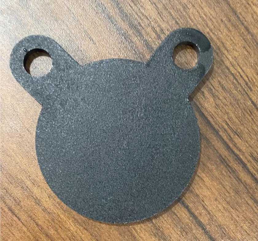 A small black AR500 3-Inch Gong Target by Yankee Thunder, resembling a bear's face with two round ears that have holes in them, placed on a wooden surface.