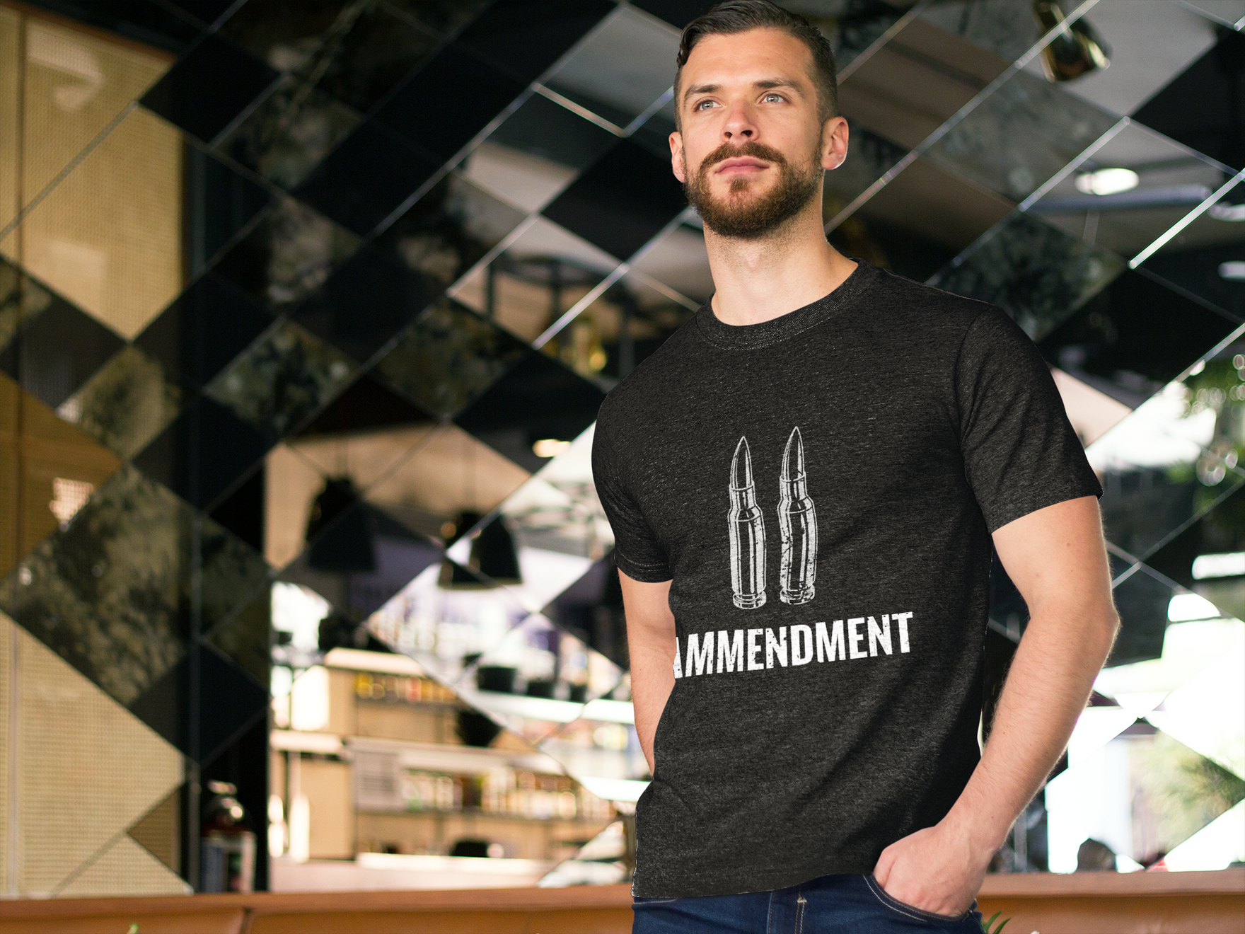 A man with short hair and a beard stands indoors in front of a reflective, patterned wall. He is dressed in a dark Yankee Thunder 2nd Amendment Tee, which features two bullet illustrations above the words 